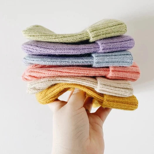 This picture shows a stack of colourful winter hats in the colours, Lime green, lilac, light blue, sorbet pink, beige and mustard yellow. 