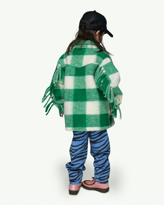 THis picture shows a girls wearing a checked wool overskirt for kids. With fringes at the front and the bottom of the sleeves. Available up to 10 years.