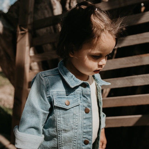 This picture shows a blue denim jacket for kids with sturdy buttons at the front. Made from Organic cotton and available up until 6 years.