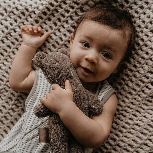 This picture shows a baby with an organic cotton baby soft toy. A brown bear with sensory tags for extra comfort and solace.