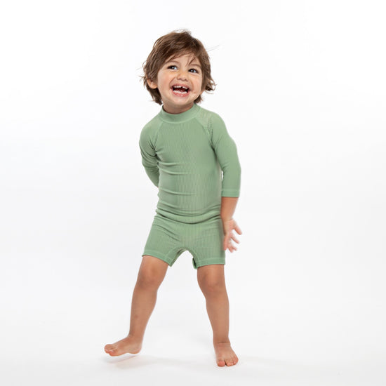This picture shows a boy wearing the ribbed basil, UPF50+ baby swimsuit