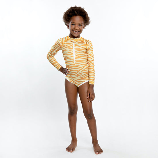 This picture shows a girl wearing an UPF50 Longsleeve swimsuit for girls in a beautiful golden tiger stripe print.