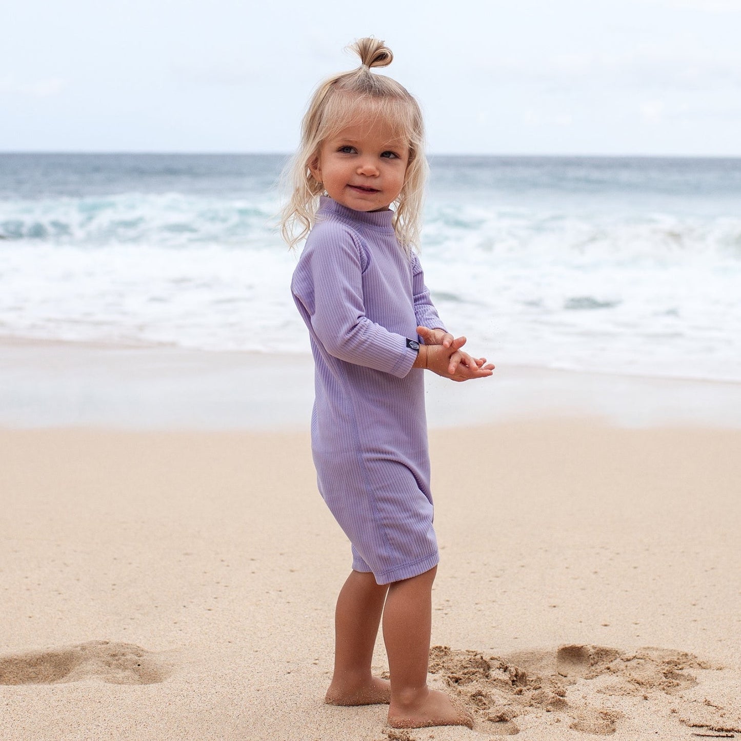 This picture shows a little girl wearing the ribbed lavender, UPF50+ baby swimsuit