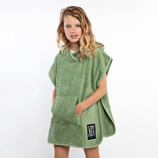 This picture shows a child wearing a beach poncho made out of 100% organic cotton in the colour basil
