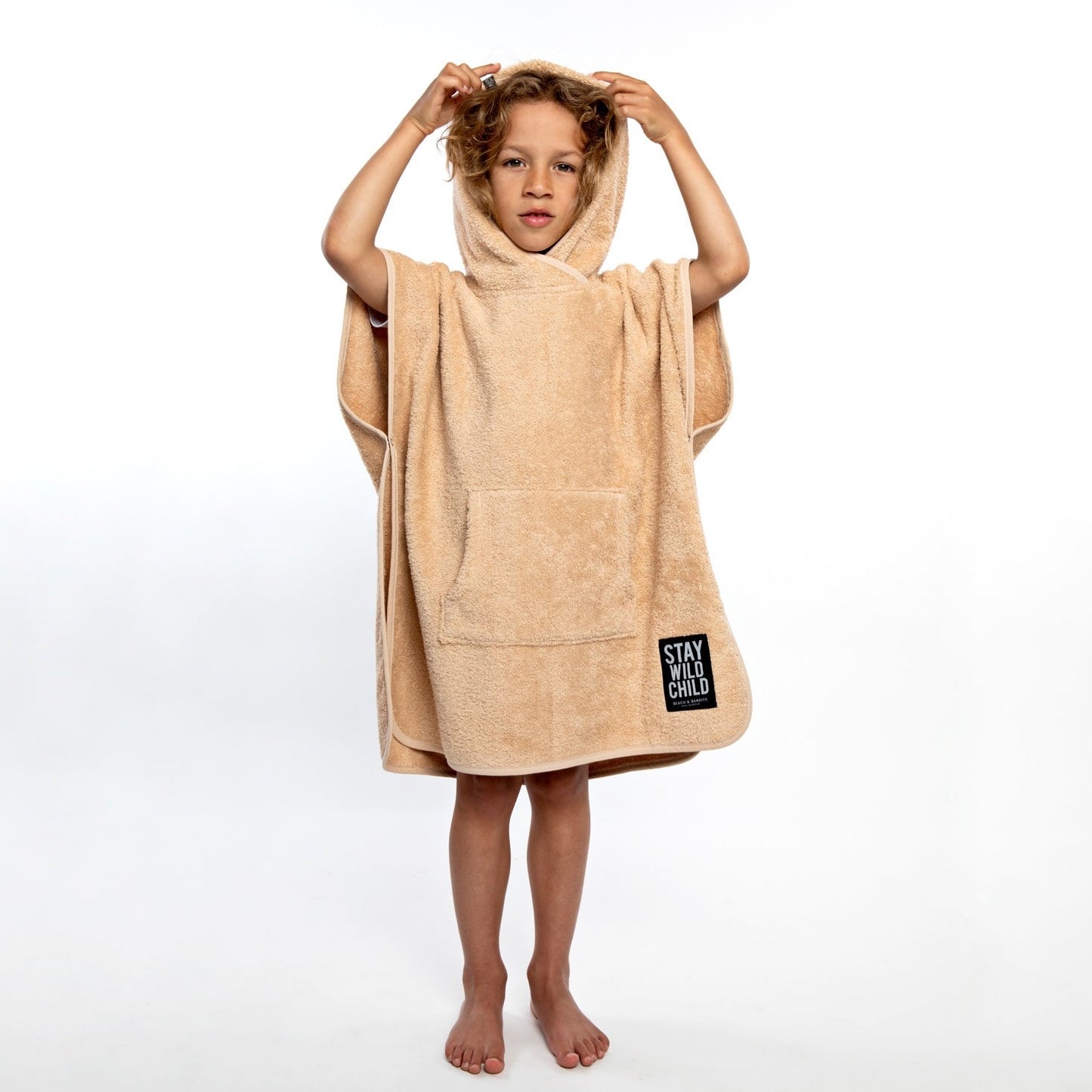 This picture shows a boy wearing a beach poncho made out of 100% organic cotton in the colour sand. 