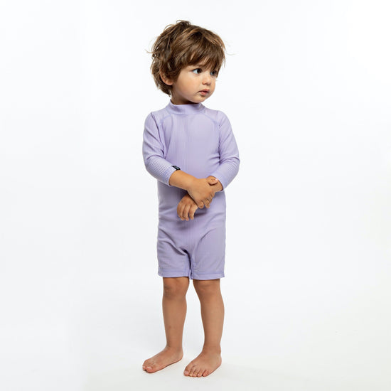 This picture shows a boy wearing the ribbed lavender, UPF50+ baby swimsuit