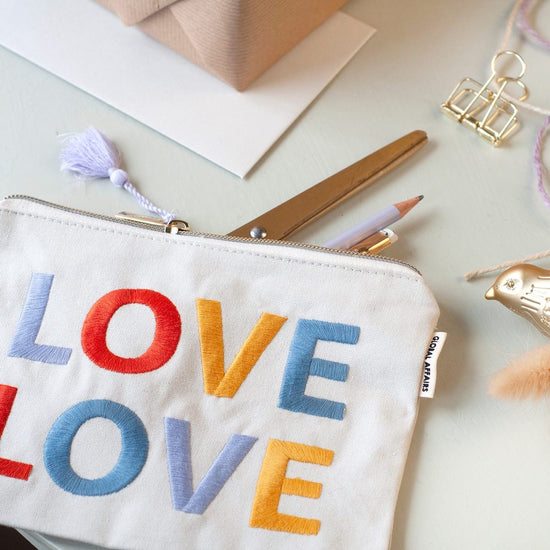 White pouch, with colourful embroidery and a lilac tassel. Love