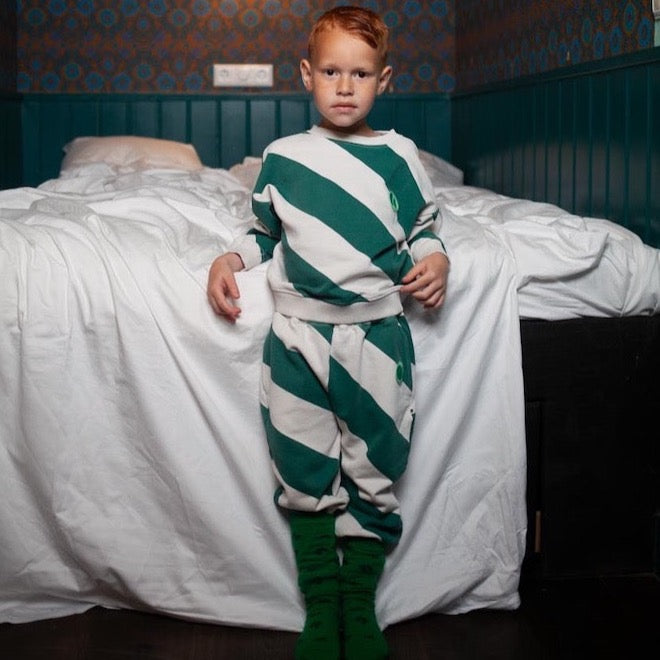 This pictures shows a boy wearing a comfy crewneck kids sweater with green big diagonal stripes and a small embroidered logo on the chest.