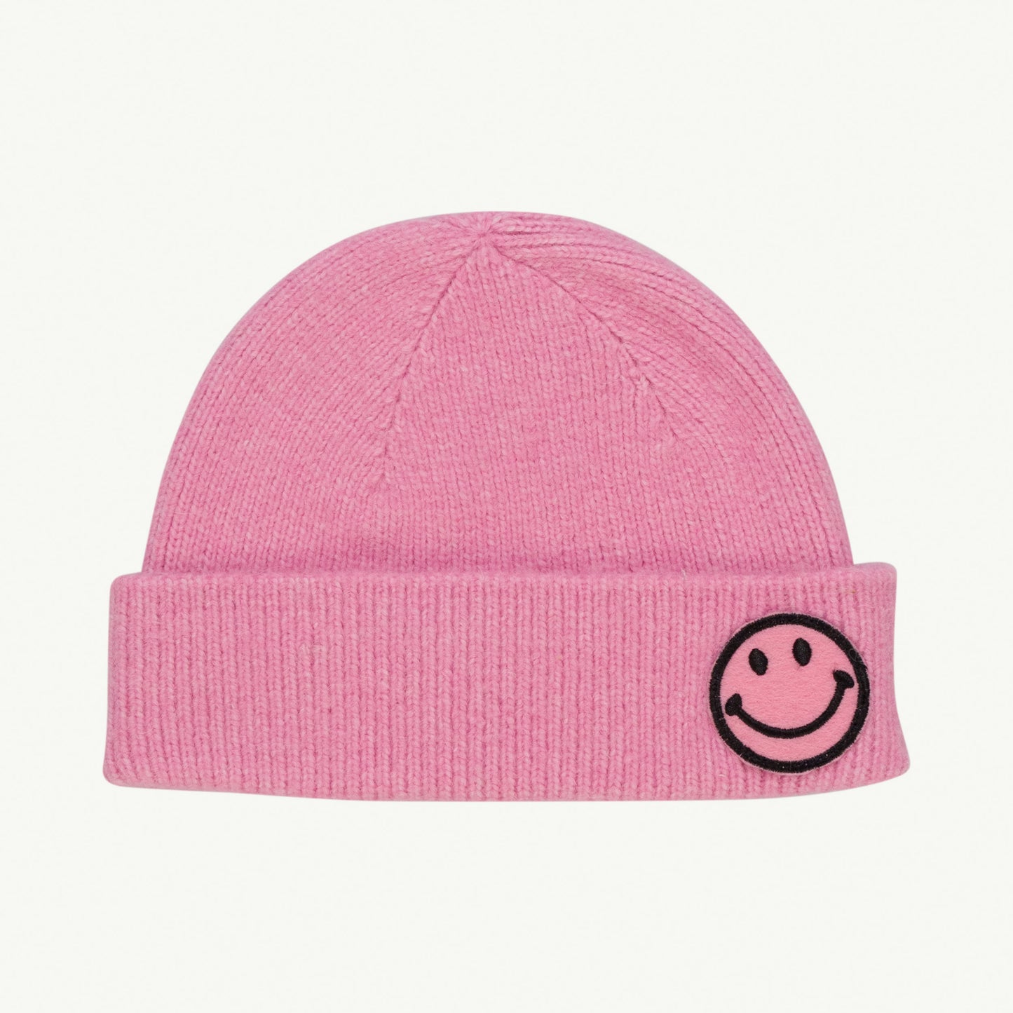 This picture shows a soft knitted pink beanie with a funny smily patch. 