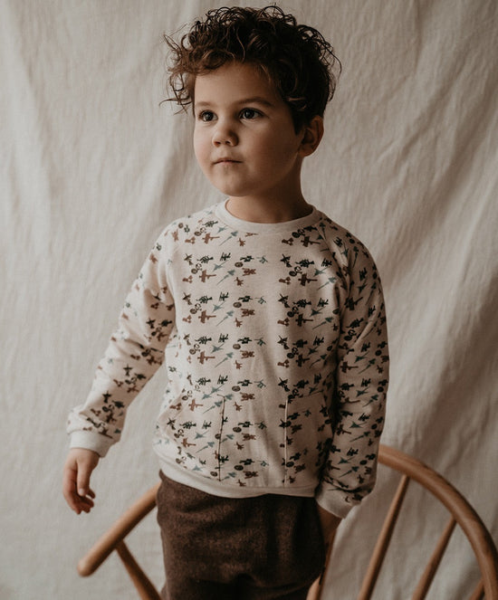 This picture shows a child wearing a off white sweater with 2 front pockets. It has green, red, blue nasca print. It is made out of 100% organic cotton.