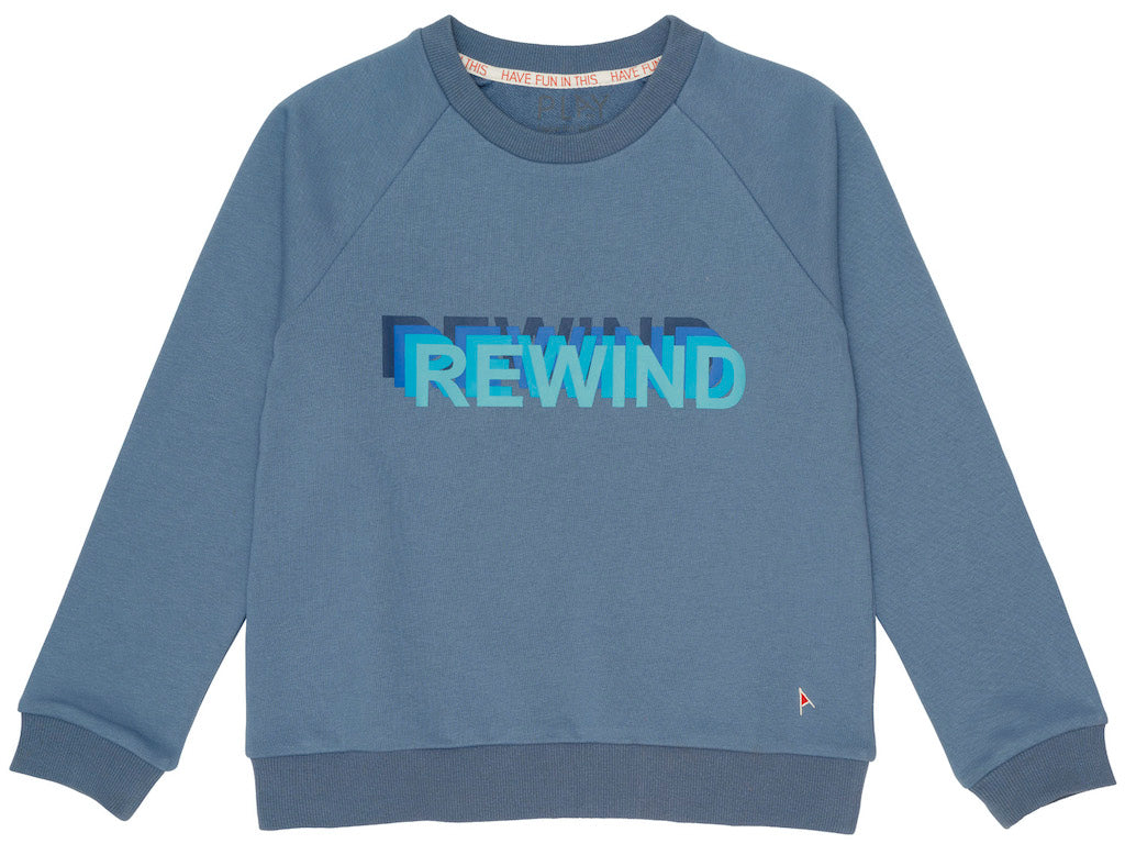 This picture shows a vintage blue kids crew neck sweater. With  rewind written on the front with graphic letters