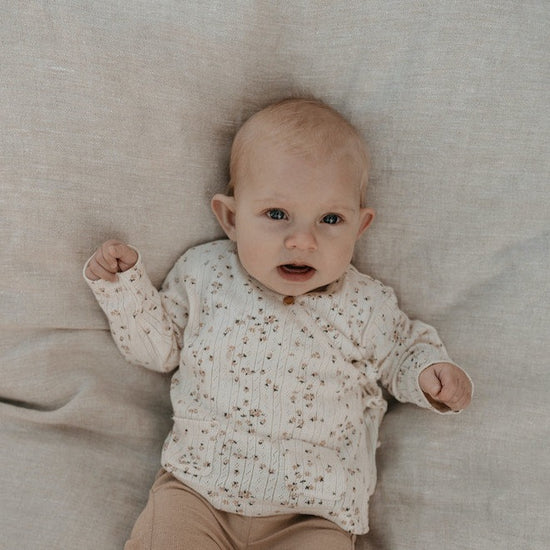 This picture shows a baby wearing the organic off white baby cardigan with a beautiful flower print. 