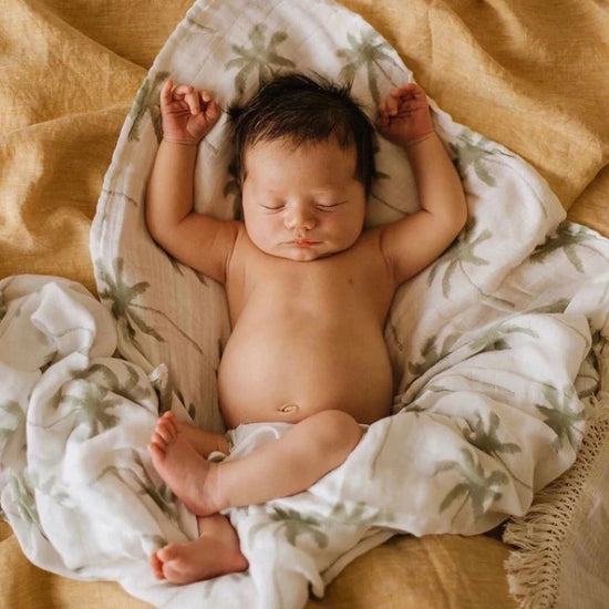 This picture shows a baby sleeping on the cotton/bamboo swaddle wrap with a sage palm print