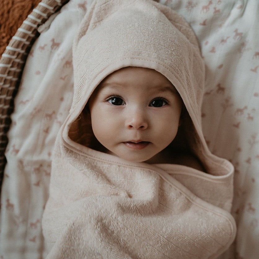 This picture show a baby wrapped in the organic cotton hooded towel. In the colour soft pink/peach. 