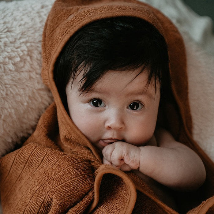 This picture shows a baby wrapped in a organic cotton hooded baby towel. IN the colour toffee
