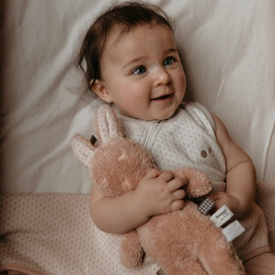 This picture shows a baby with a soft toy bunny in pink. Sensory tags on the side fro extra comfort