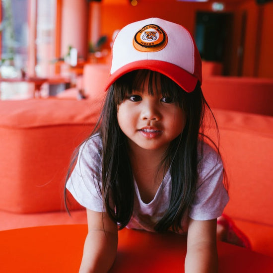 This picture shows a girl wearing the red sporty kids cap with a mesh back and a adjustable strap. Cool tiger badge on the front.